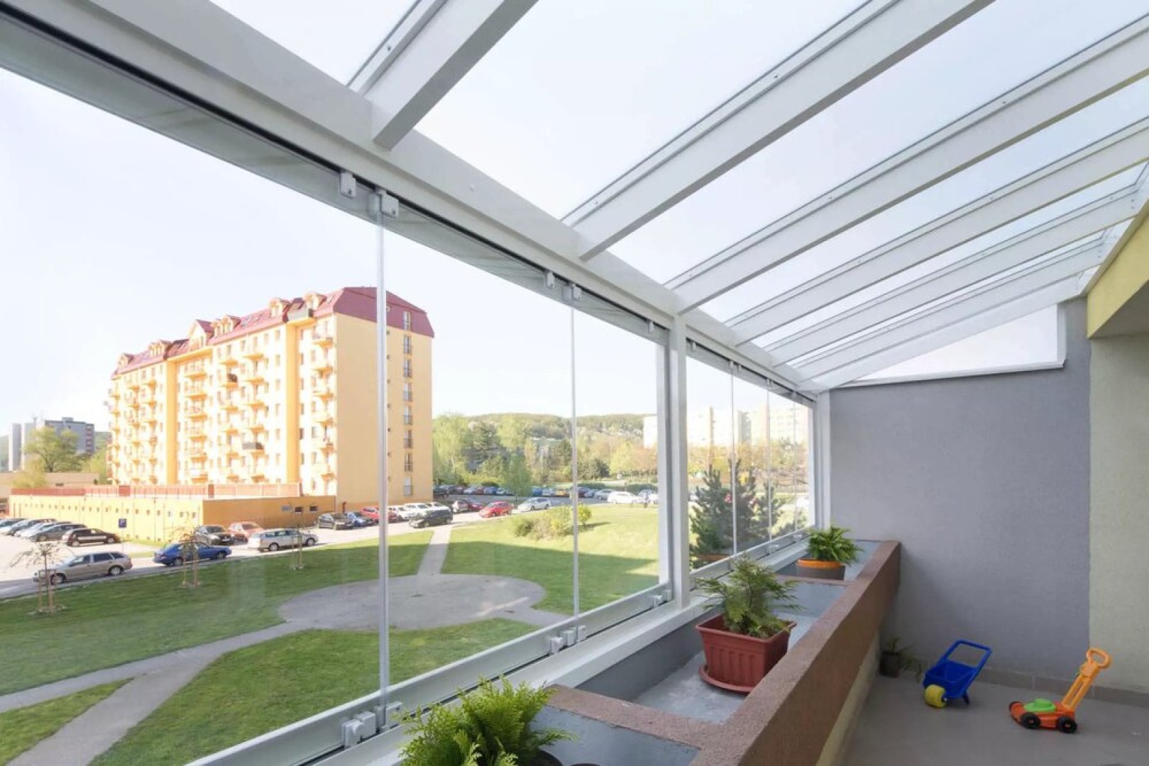 Moderné bezrámové zasklenie balkóna s výhľadom na sídlisko a zeleň